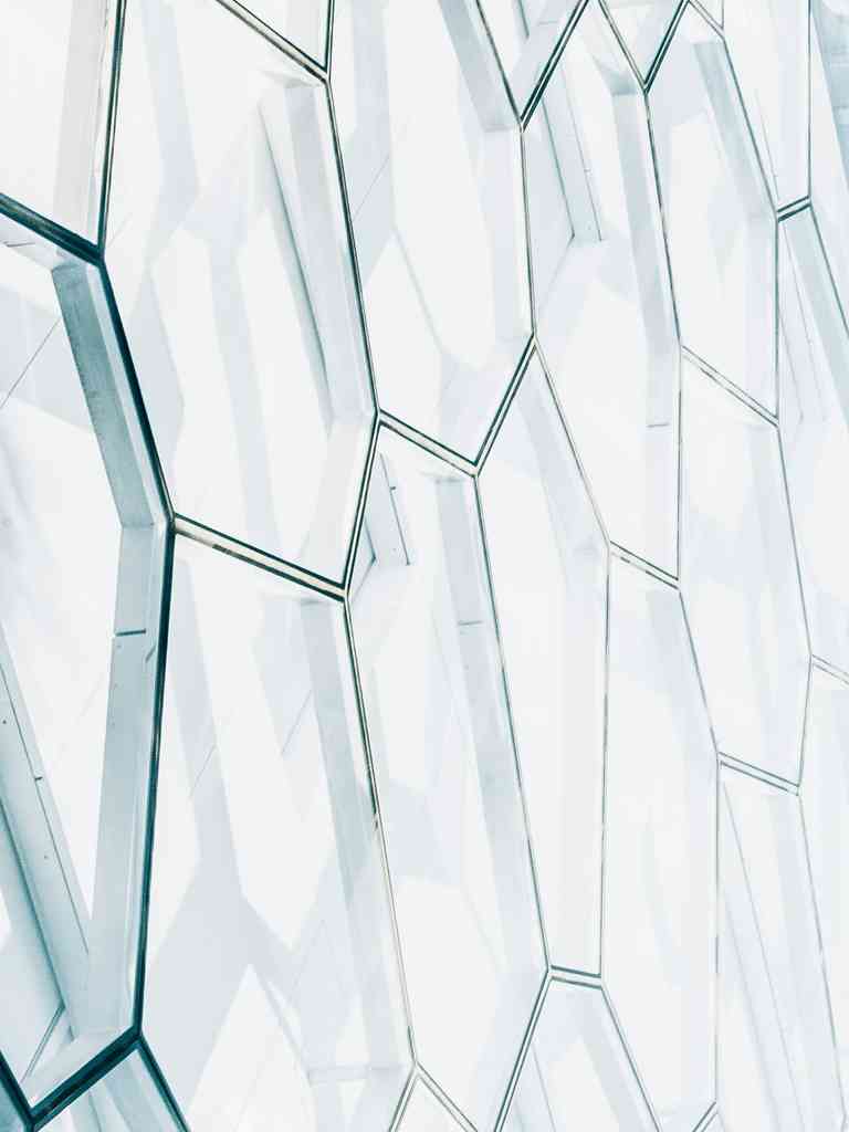 Modern glass building facade with geometric hexagonal window panels viewed from below against a clear sky.